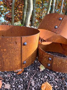 two rusted metal planters sitting on top of a gravel ground next to trees