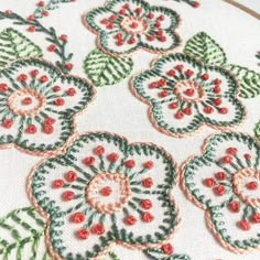 a close up of a cross stitch pattern on a piece of cloth with red and green flowers