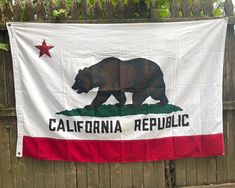 a california flag hanging on a fence with a bear in the center and stars above it