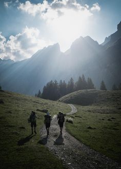 three people walking down a trail in the mountains with backpacks on their back,