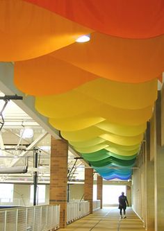 a man walking down a long hallway with lots of colorful balloons hanging from the ceiling