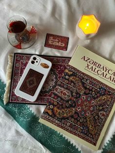 an open book sitting on top of a bed next to two candles and a cell phone