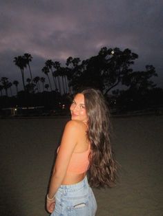 a woman standing on top of a sandy beach at night with palm trees in the background