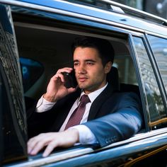 a man in a suit and tie talking on a cell phone while sitting in a car