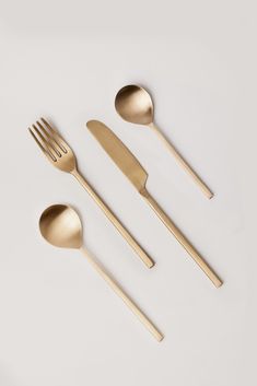 three gold spoons, two forks and one knife on a white surface with copy space