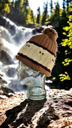 a knitted hat sitting on top of a head in front of a mountain waterfall