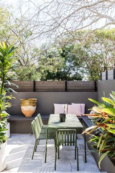 an outdoor dining area with green chairs and plants on the table, surrounded by greenery