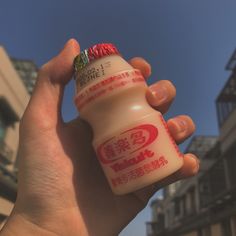 a hand holding a small bottle with chinese writing on the side and buildings in the background