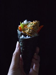 a hand holding up a sushi with rice, carrots and other toppings