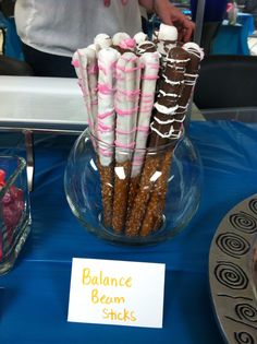 there are some candy sticks in a glass bowl on the table with a sign that says balance beam sticks