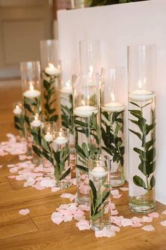 candles are lined up in glass vases with leaves and flowers on the floor next to them