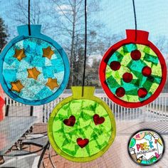 three colorful glass ornaments hanging from strings on a window sill with trees in the background