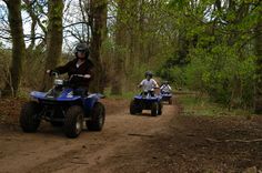 three people riding four wheelers on a dirt road