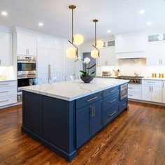 a large kitchen with white cabinets and blue island in the center, surrounded by wood flooring