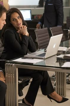 two people sitting at a table with laptops in front of them and one person on the phone