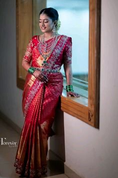 a woman in a red and gold sari standing next to a window with her hands on her hips