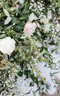 white flowers and greenery are arranged on a table