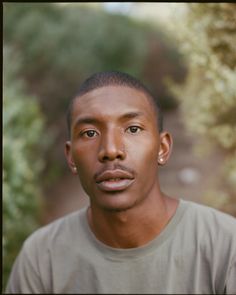 a young man is looking at the camera with an intense look on his face as he stands in front of some bushes