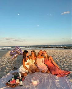 three women sitting on the beach with balloons and cake