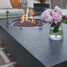 a fire pit sitting on top of a table next to a vase filled with flowers