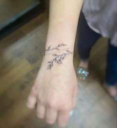 a small tattoo on the wrist of a woman's left hand, with flowers and leaves