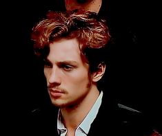 a man with curly hair wearing a black jacket and white shirt is looking at the camera