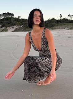 a woman kneeling on top of a sandy beach next to the ocean with her legs spread out