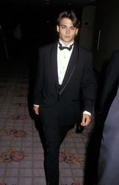 a young man in a tuxedo and bow tie walking down a hall way