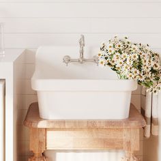 a white sink sitting on top of a wooden table next to a mirror and vase with flowers