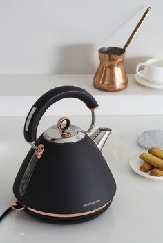 a black tea kettle sitting on top of a white counter next to some plates and cups