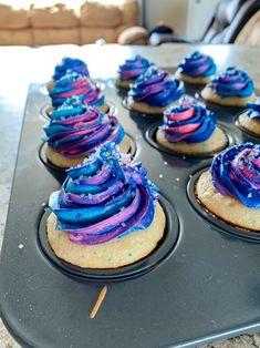 cupcakes with blue and purple icing in a muffin tin on a counter