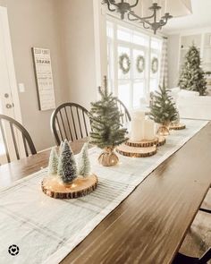 a dining room table decorated for christmas with small trees on the centerpiece and candles