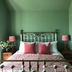 a bed with pink and white pillows in a green room next to two nightstands