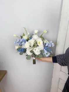 a woman holding a bouquet of white and blue flowers in front of a door handle