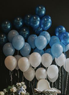 a bunch of blue and white balloons hanging from the side of a table with greenery