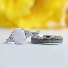 two wedding rings with opal and diamond accents on a white surface next to a yellow flower