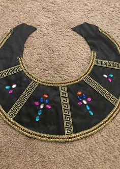 a black bib with multi colored beads on it sitting on the floor next to a carpet