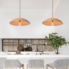 three hanging lights above a kitchen island with chairs and plates on the counter, next to a potted plant