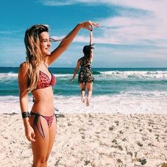 two women in bikinis on the beach playing frisbee