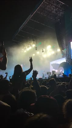 a crowd at a concert with their hands in the air and lights shining down on them