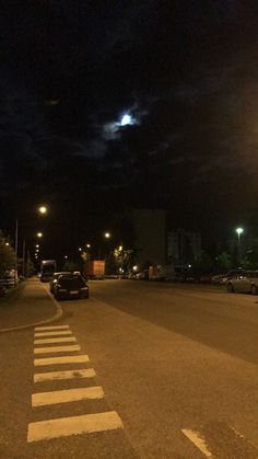 cars are parked on the side of an empty street at night with moon in the sky