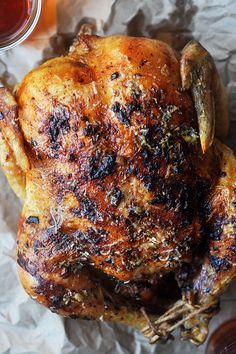 a roasted chicken on wax paper next to a cup of tea and some sauces