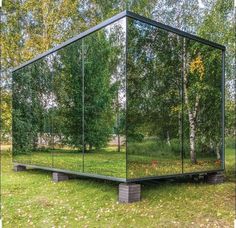 a mirrored box sitting in the middle of a field with trees and grass around it