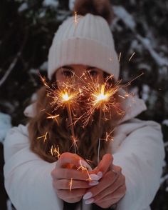 a woman holding sparklers in her hands while wearing a white hat and coat with snow on the ground