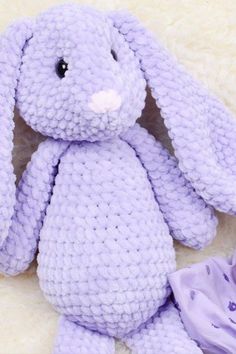 a purple crocheted stuffed animal sitting on top of a white blanket next to a purple flower