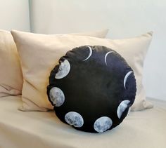 a black pillow with white phases on it sitting on a bed next to two pillows