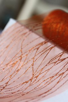 a close up of a piece of cloth with gold thread on it and a red object in the background