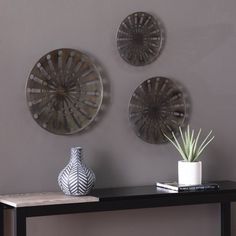 three circular metal wall hangings on the wall above a table with a plant and vase