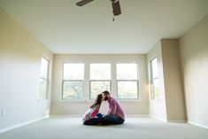 a man and woman sitting on the floor in an empty room with two large windows