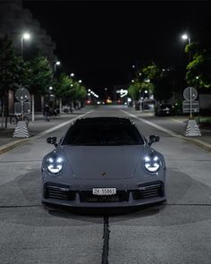 a grey sports car parked in the middle of an empty street at night with lights on